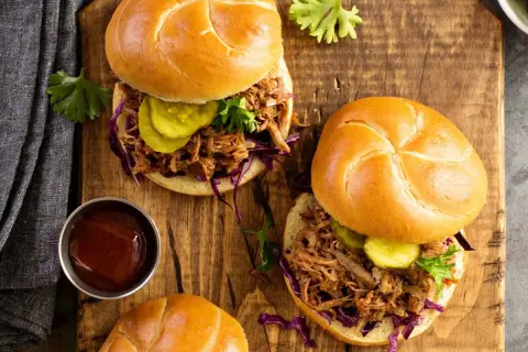 Dos jugosos sándwiches de pulled pork con pepinillos y col morada sobre pan rústico, listos para disfrutar.