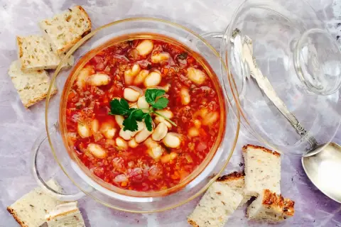 Un tazón de alubias con verduras, servido con pan rústico.