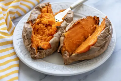 Dos mitades de boniato cocinado en freidora de aire, servidas en un plato blanco con un tenedor.