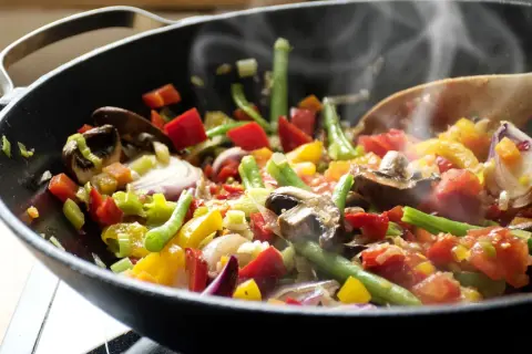 Un delicioso salteado de verduras humeante en un wok, con pimientos, judías verdes, champiñones y cebolla morada.