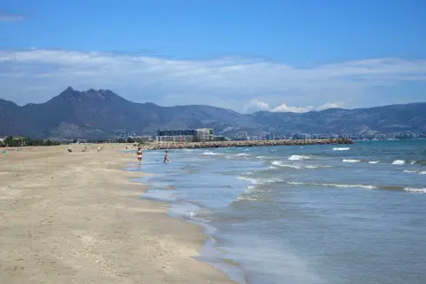 La playa del Serradal, con sus montañas al fondo, invita a pasear por la orilla mientras las olas acarician la arena dorada.