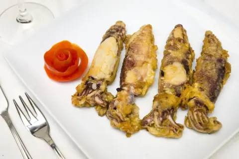 Cuatro chipirones fritos dorados y crujientes, servidos en un plato blanco con una rosa de tomate y cubiertos.