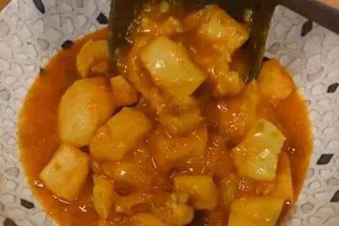 Un plato de papas con choco en una salsa naranja.