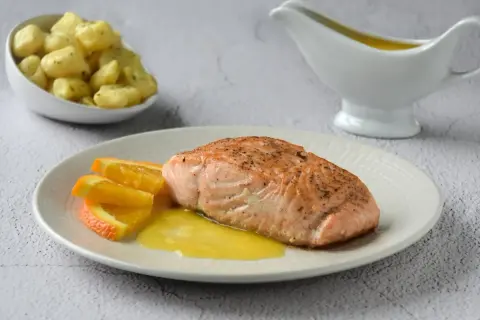 Filete de salmón a la naranja, servido con gajos de naranja y una salsa dorada. Acompaña unas patatas.