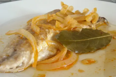 Deliciosa caballa en escabeche, con cebolla caramelizada y hoja de laurel, servida en un plato blanco.