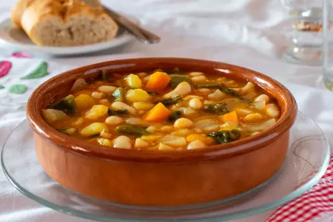 Un plato de barro con una sabrosa comida típica de Castellón: judías blancas, patatas, zanahoria y verduras en un caldo reconfortante.