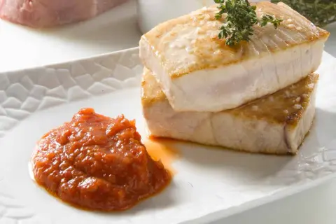 Dos trozos de atún a la plancha apilados, con una guarnición de salsa de tomate y una ramita de tomillo.