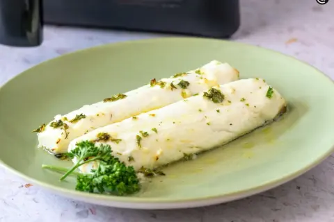 Dos filetes de merluza jugosa, recién hechos en airfryer, con hierbas frescas y aceite de oliva.
