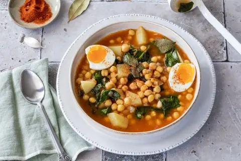 Un reconfortante plato de garbanzos con espinacas, patatas y huevos duros, espolvoreado con pimentón.