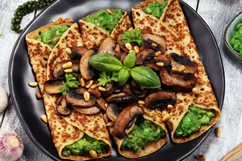 Crepes salados rellenos de aguacate y champiñones salteados, decorados con piñones y albahaca fresca.