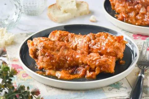 Muslos de pollo en salsa, una receta de la abuela que evoca recuerdos de hogar. Servidos en un plato oscuro, con pan y un tenedor.