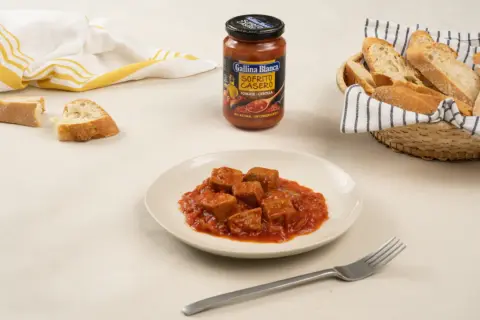 Sabroso atún con tomate en un plato, acompañado de pan y un sofrito casero de Gallina Blanca.