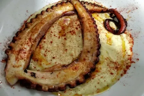 Tentáculos de pulpo a la plancha, dorados y tiernos, servidos sobre puré cremoso y espolvoreados con pimentón.