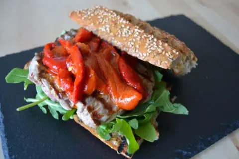 Un delicioso pepito de ternera con pimientos rojos asados y rúcula, servido en pan rústico con semillas.