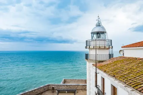 El faro de Peñíscola se alza vigilante sobre el mar turquesa, con un cielo nublado que promete aventura.