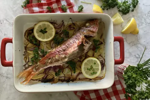 Deliciosos salmonetes al horno con patatas, cebolla roja, limón y perejil fresco, listos para servir.