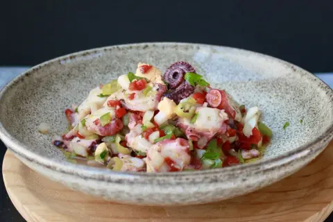 Salpicon de pulpo fresco con pimientos, cebolla y perejil, servido en un cuenco rústico.