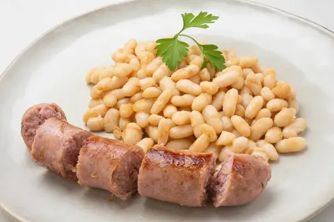 Un plato de alubias blancas tiernas y jugosas salchichas, decorado con una ramita de perejil fresco.