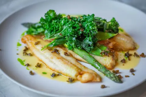 Filetes de bacalao en salsa verde, acompañados de espárragos y kale crujiente.