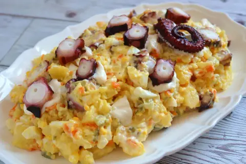 Deliciosa ensaladilla de pulpo con patatas, huevo y zanahoria, coronada con trozos de pulpo tierno y un toque de mayonesa.