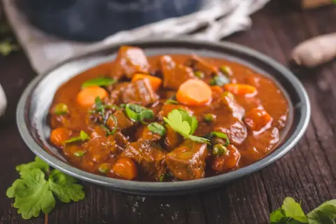 Un plato humeante de rabo de ternera estofado con zanahorias y guisantes, adornado con perejil fresco.