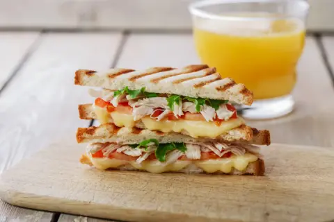 Delicioso sandwich de pollo a la parrilla con queso derretido, tomate y lechuga, acompañado de un vaso de jugo de naranja.