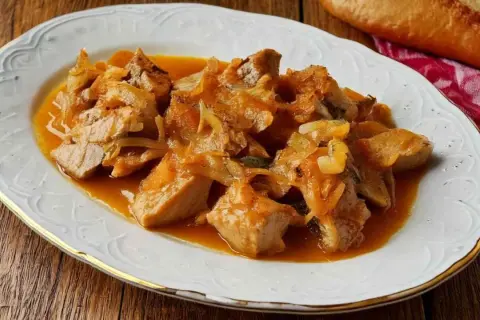 Sabroso atún encebollado en una salsa dorada, servido en un plato blanco con borde dorado.