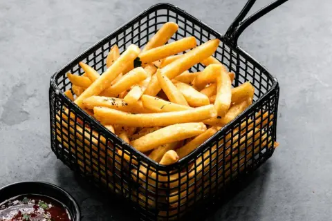 Patatas soufflé doradas y crujientes en una cesta negra, listas para ser disfrutadas con una salsa.