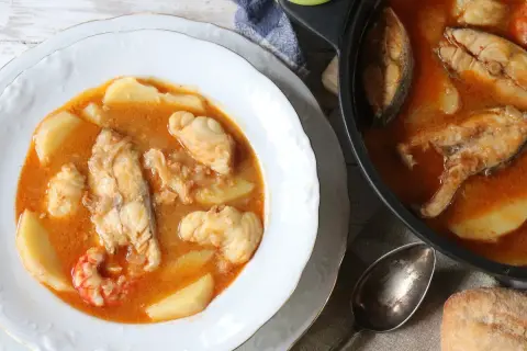 Un plato humeante de suquet de pescado, con trozos de pescado blanco, patatas y gambas en una rica salsa.
