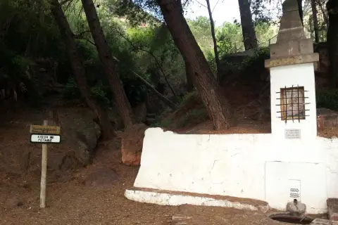 En la ruta de las fuentes, un cartel indica "AIGUA NO POTABLE" junto a una fuente de piedra y un pequeño altar en un bosque.
