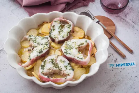 Rodajas de pescado rosado al horno con patatas, cubiertas de hierbas frescas.