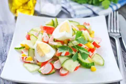 Deliciosa ensalada de cangrejo con pepino, huevo cocido y maíz, decorada con perejil fresco.