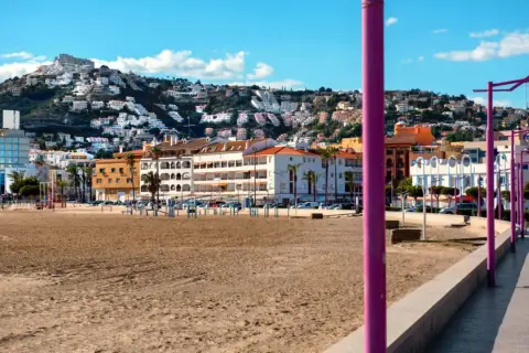 Playa de Peñíscola con el paseo marítimo y edificios blancos escalonados en la ladera de una montaña.