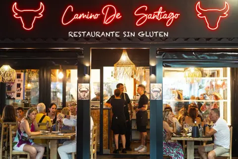 Restaurante "Camino de Santiago" en Peñíscola, con letrero de neón y comensales disfrutando de una comida.