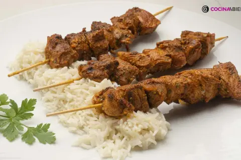 Tres pinchos morunos jugosos sobre una cama de arroz blanco, decorados con perejil fresco.