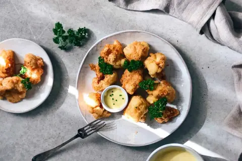 Crujiente coliflor rebozada, dorada y servida con salsa de mostaza y perejil fresco. ¡Un aperitivo delicioso!