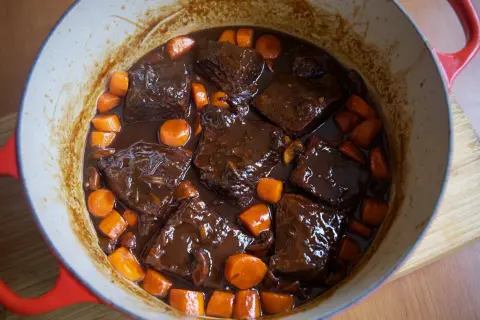 Boeuf bourguignon cocinado a fuego lento en una olla roja, con trozos de carne tierna, zanahorias y champiñones en una rica salsa.