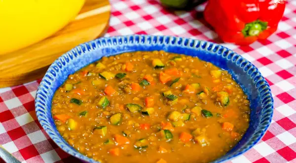Un plato azul con un guiso de lentejas, zanahoria y calabacín. Una idea deliciosa de como hacer lentejas.