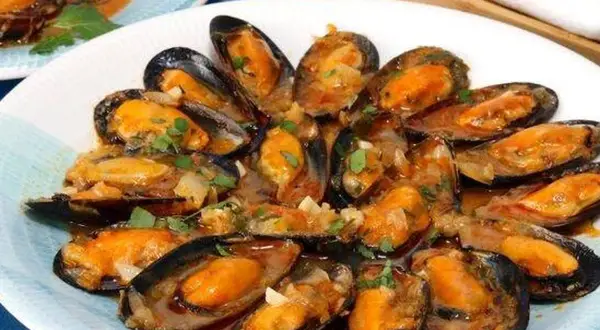 Un plato de mejillones a la marinera, jugosos y con una salsa sabrosa, adornados con perejil fresco.