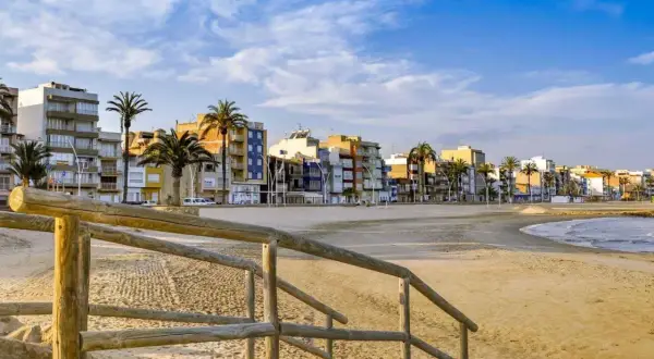 Escaleras de madera bajan a una playa vacía con edificios coloridos y palmeras al fondo. Un ejemplo de pueblos bonitos cerca de Benicàssim.