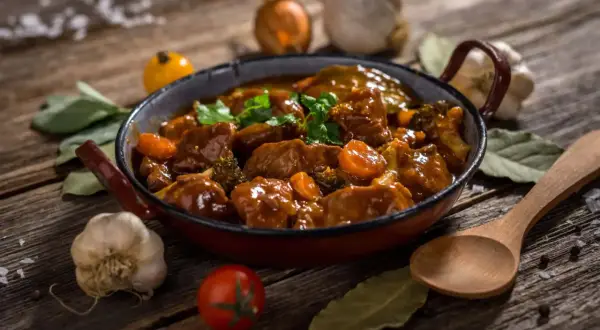 Un delicioso ragout de ternera, con trozos de zanahoria y brócoli, servido en una sartén rústica. Acompañado de ajo, tomate y laurel.