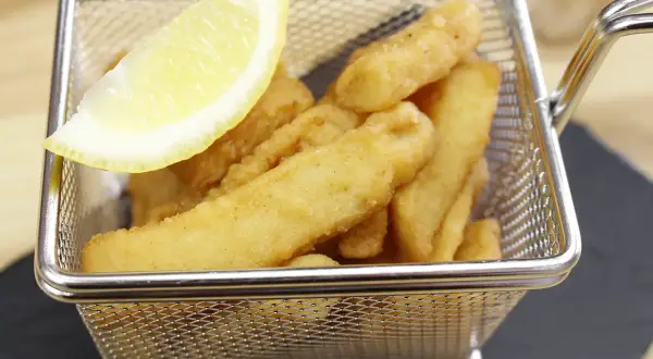 Deliciosos chocos fritos crujientes en una cesta metálica, acompañados de una rodaja de limón.