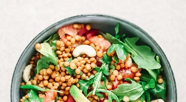 Deliciosa ensalada de lentejas con aguacate, tomate y rúcula, coronada con anacardos. Un plato fresco y nutritivo.