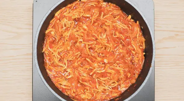 Tinga de pollo cocinándose en una sartén, con trozos de pollo deshebrado y salsa roja.