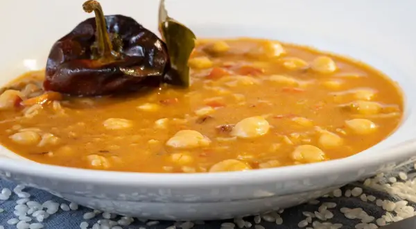 Un plato humeante de garbanzos con arroz, decorado con un pimiento seco y una hoja de laurel.