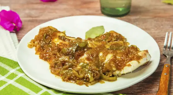 Un plato de urta a la roteña, con su jugoso pescado cubierto de cebolla y pimientos caramelizados, listo para disfrutar.