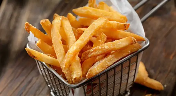 Cesta metálica llena de crujientes patatas fritas al horno, servidas sobre papel blanco.