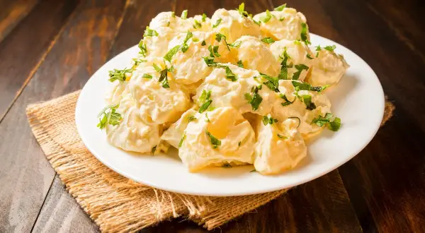 Patatas alioli cremosas y deliciosas, cubiertas con perejil fresco, servidas en un plato blanco sobre una mesa de madera rústica.