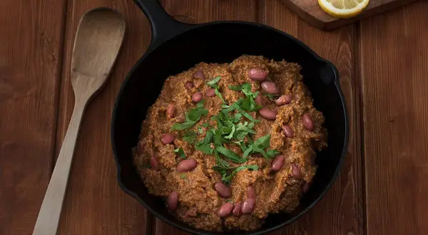 Un delicioso chili con carne humeante en sartén de hierro fundido, adornado con frijoles rojos y cilantro fresco.