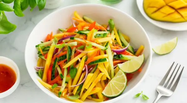 Ensalada de mango vibrante con pepino, zanahoria, cebolla morada y pimientos, aderezada con lima.